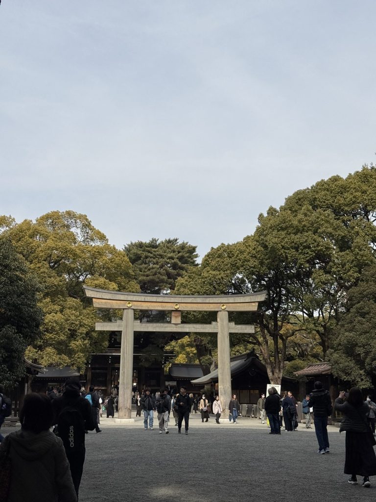 Visitors walking under the large wooden torii gate at Meiji Jingu shrine, framed by tall green trees