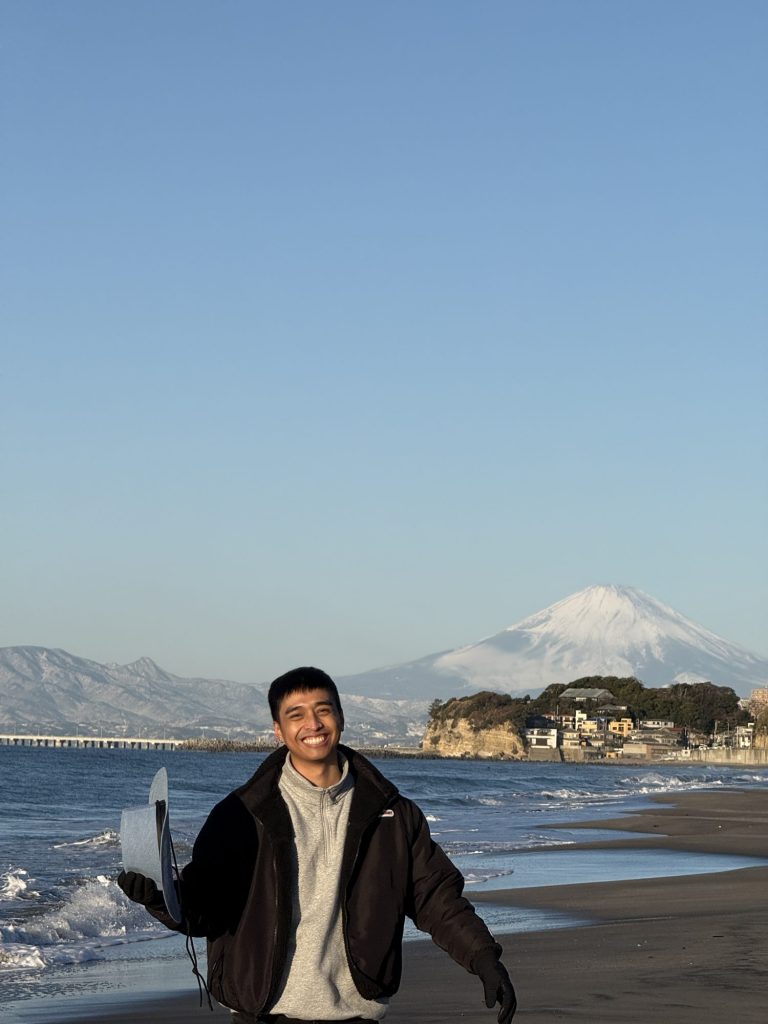 Smiling man on Shichirigahama beach at sunrise with Enoshima island and snowy Mt. Fuji across the water