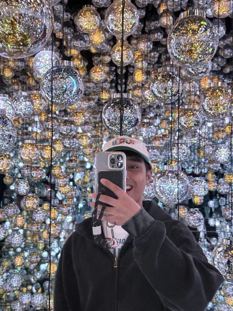 Smiling mirror selfie surrounded by hundreds of glowing glass spheres in the Bubble Universe room at teamLab Borderless