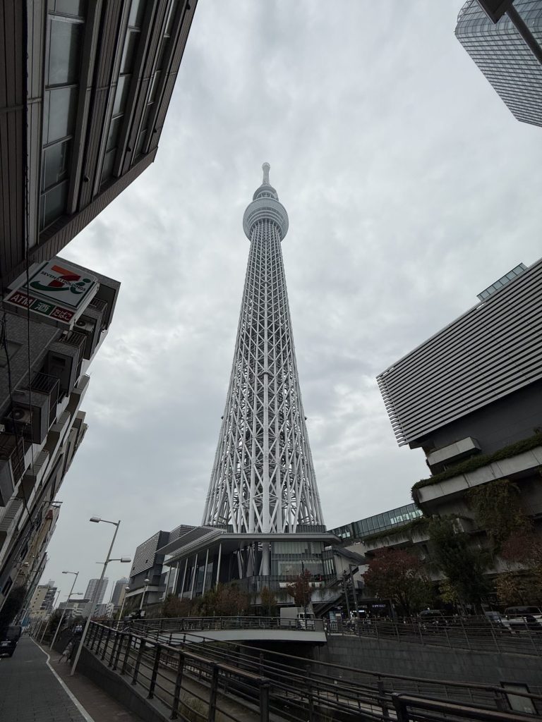 Looking straight up at Tokyo Skytree from the street on a cloudy day, framed by nearby buildings